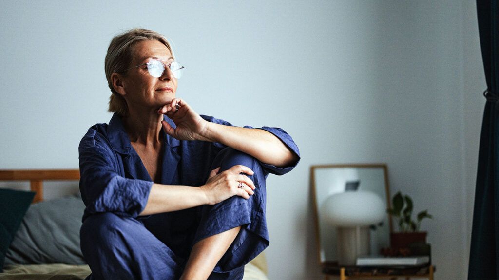 Older woman sitting on bed looking into distance