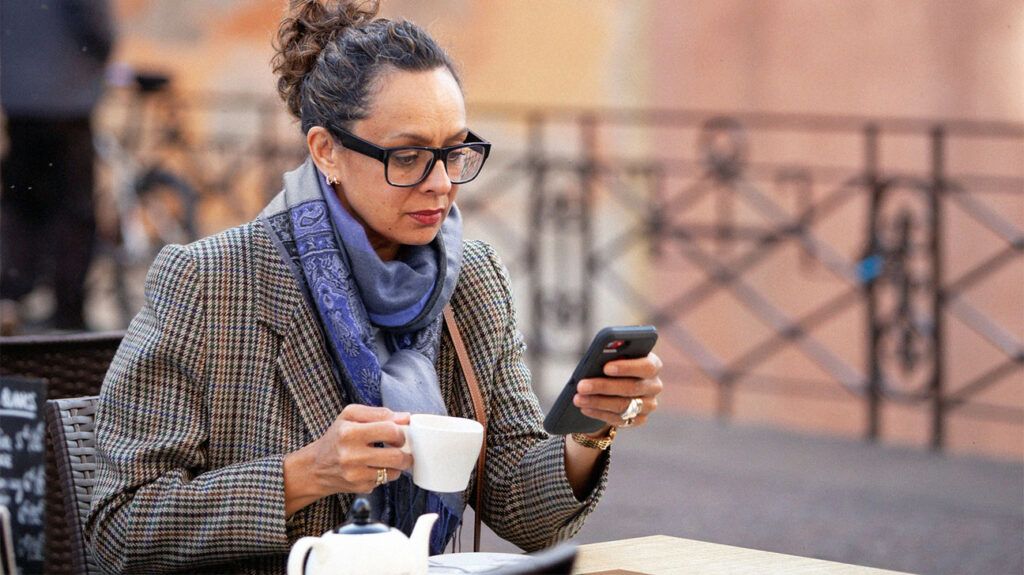 mature white woman wearing tweed blazer and glasses looking at her phone