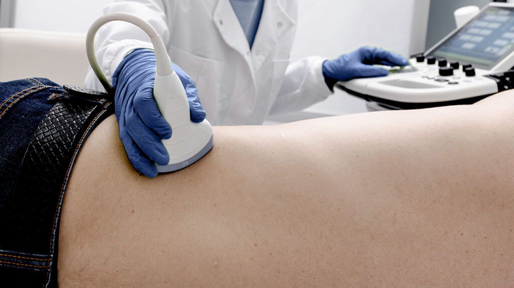A healthcare professional moving an ultrasound transducer over the area of the kidneys