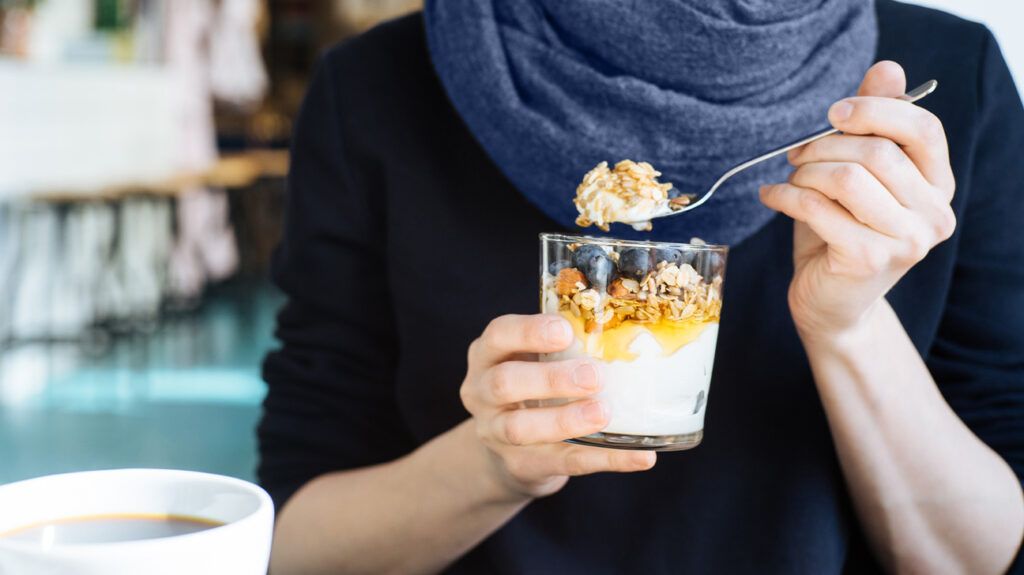 a person eating a glass of yogurt and granola