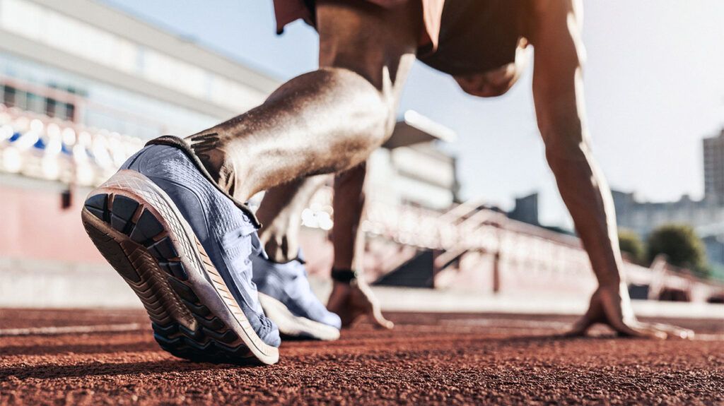 Close up of male athlete getting ready to start running on track . Focus on sneakers