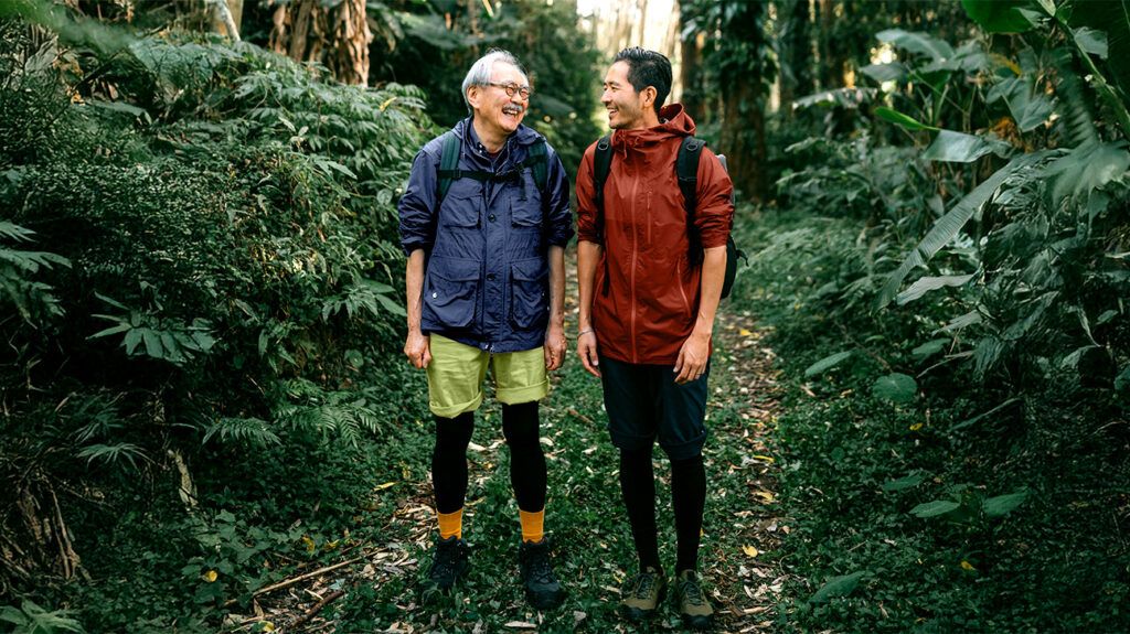 older man and younger man smiling at each other in a forest