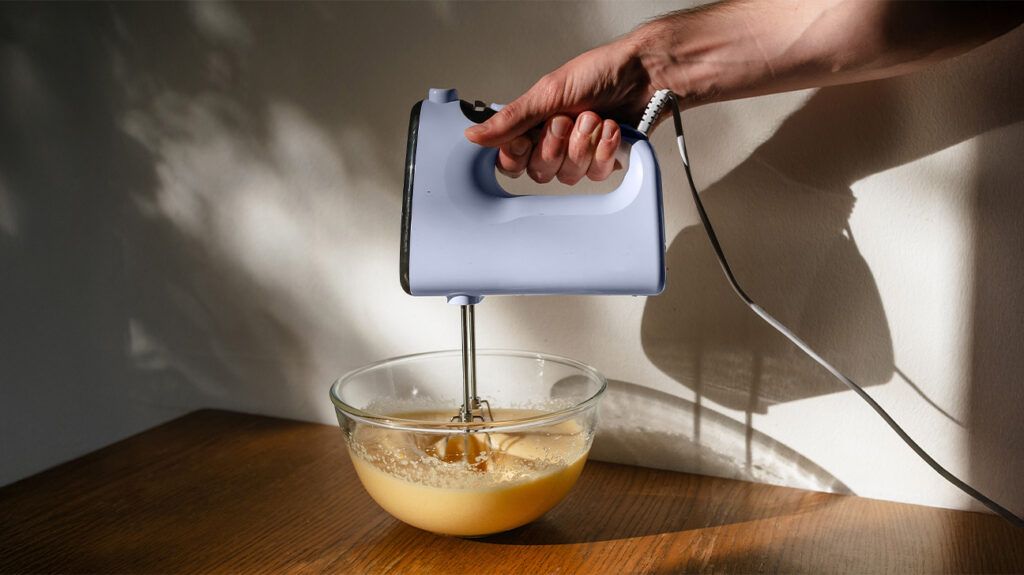 a person holding a hand held mixer in a bowl
