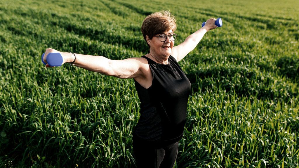 older white woman lifting hand weights in a field
