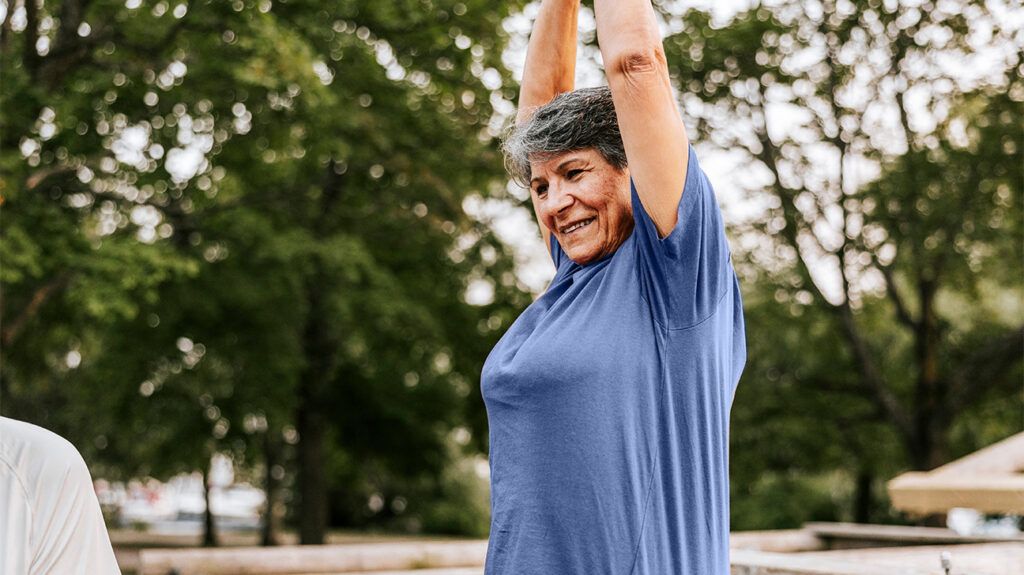 An older woman stretching her arms above her head outside