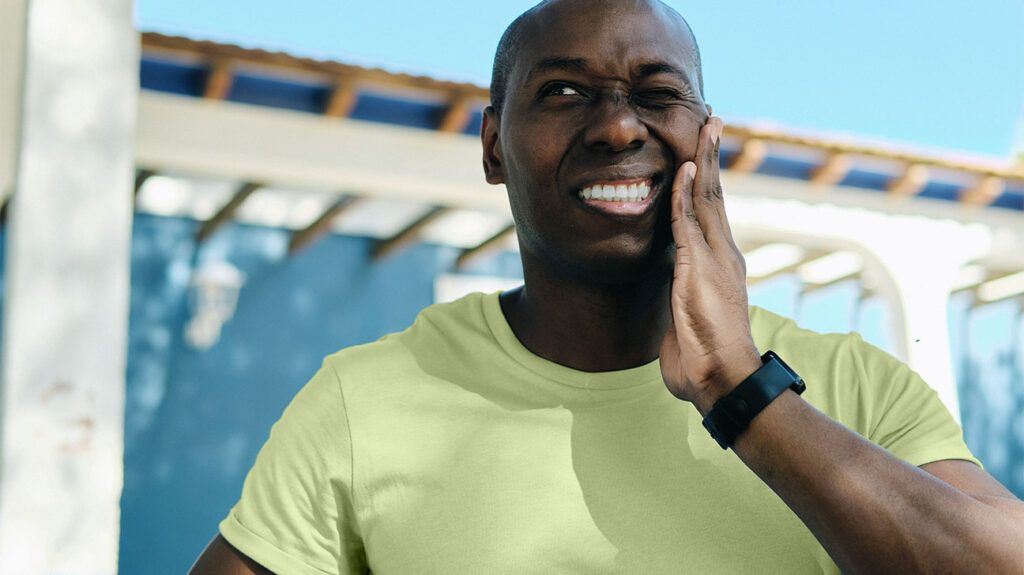 Young 35s-40s man experiencing jaw pain outdoors.