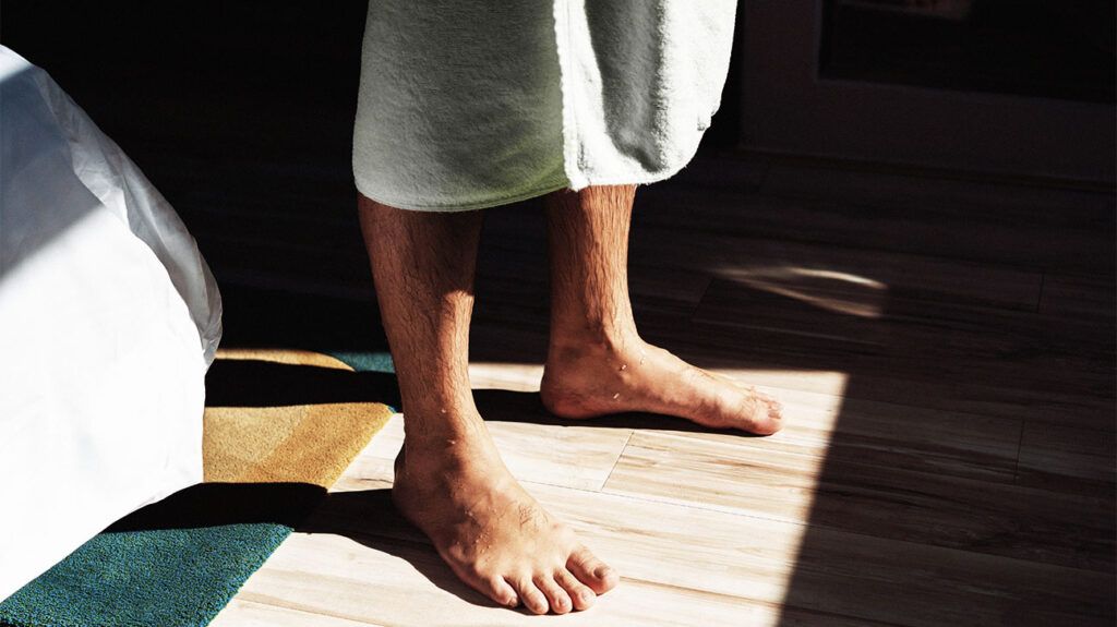 The lower body of a man standing on a bath mat in a towel after showering.