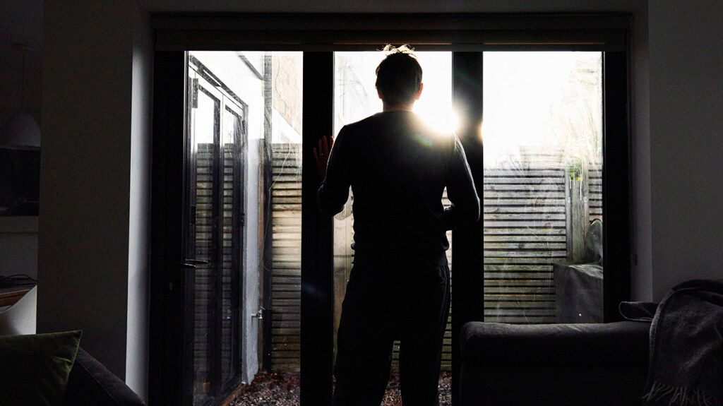 The silhouette of a man looking through a window into his garden. -2