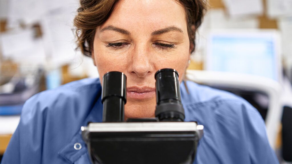 A healthcare professional looking through a microscope lens.-1
