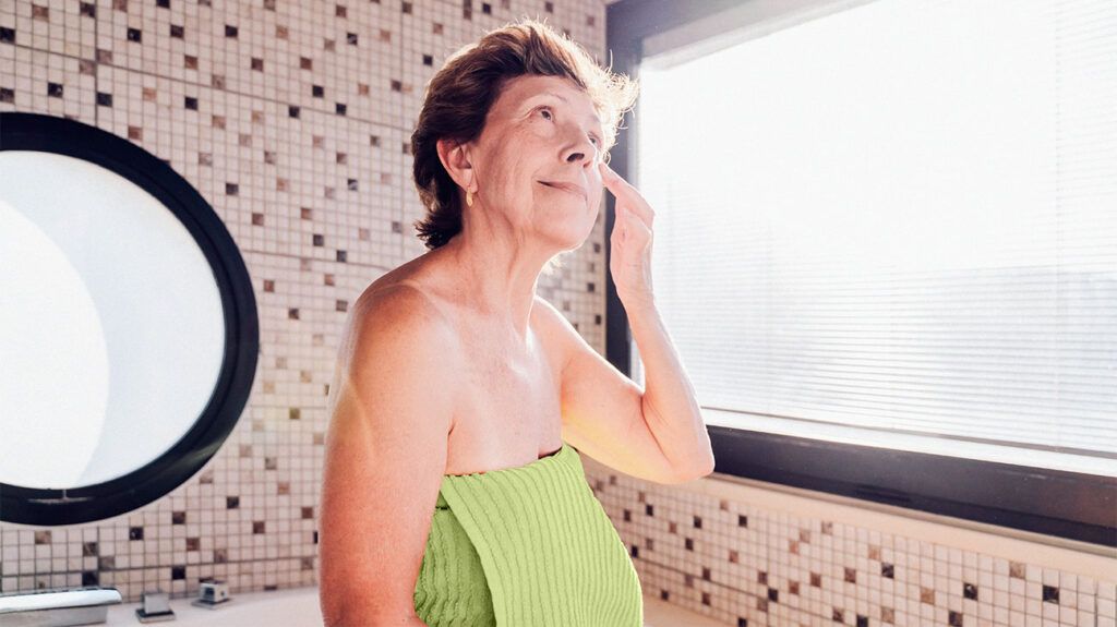 A person in a towel gets a facial massage in a bathroom after shower.