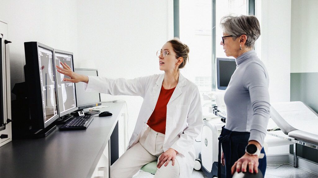 Female doctor and senior patient discuss medical images on computer monitors-1