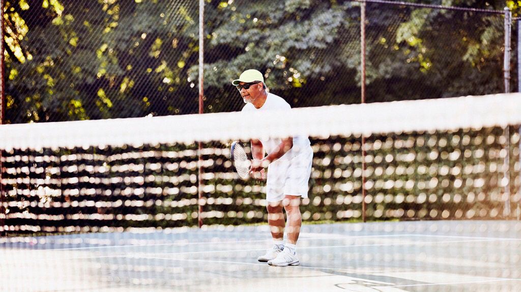 Senior man playing at net during early morning tennis match. -2