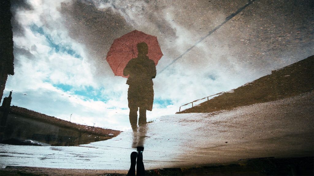 우산을 쓴 사람이 비 속을 걷고 있는데 땅에 있는 웅덩이에 그
사람의 모습이 비친다.<BR>