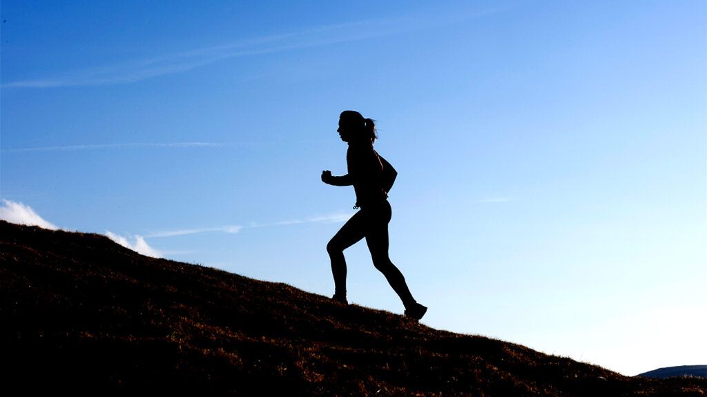 silhouette of person with ponytail running uphill