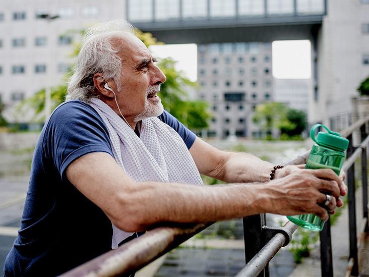 Older adult man holding a water bottle and towel outdoors.