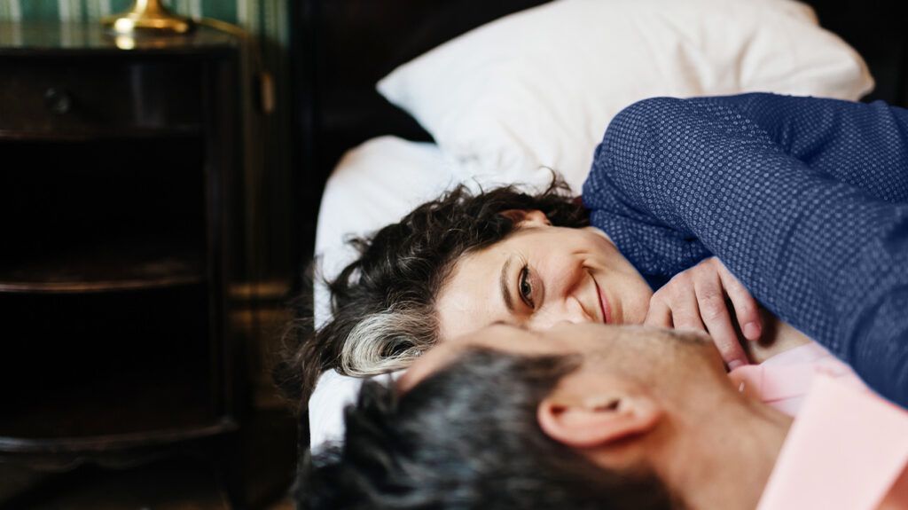 A woman and men lying next to each other on a bed smiling.
