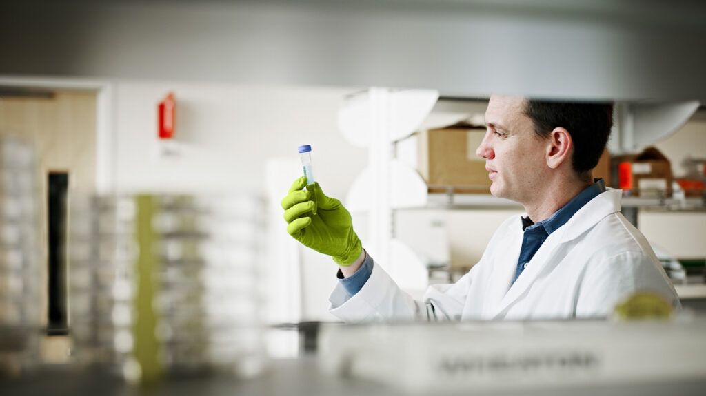 a person in a lab coat holding a vial up to the light