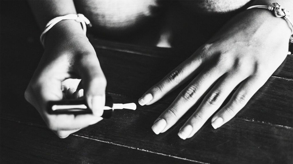close up of woman with long, slender fingers, applying product to her nails at home