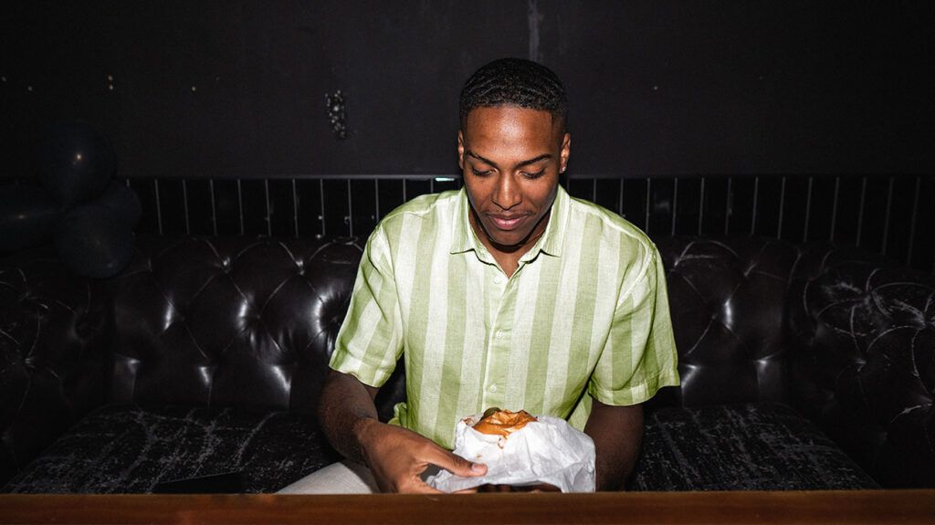 A man unwrapping a burger against a dark background.-2