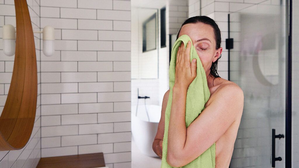 A person wiping their face with a green towel in the bathroom.-2