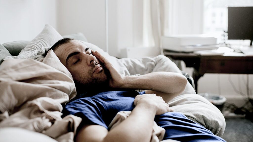 A tired man sleeping in a bed, holding his face with one of his hands