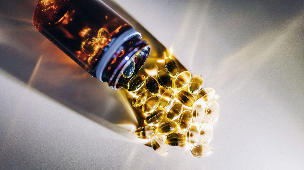 Golden vitamin D pills spilling out of a brown plastic bottle onto a white surface.