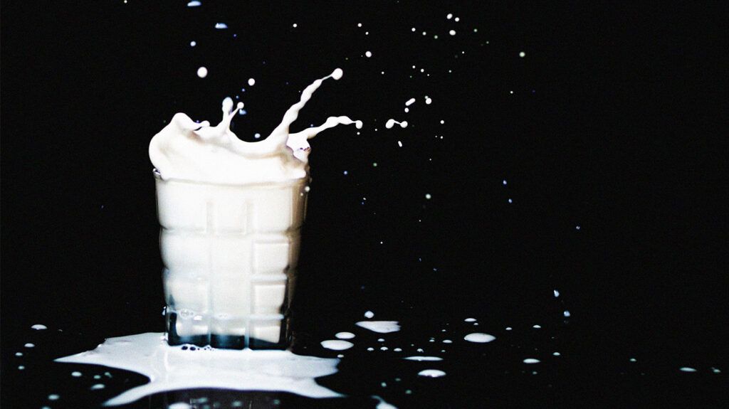 A glass of milk splashing on a black background.