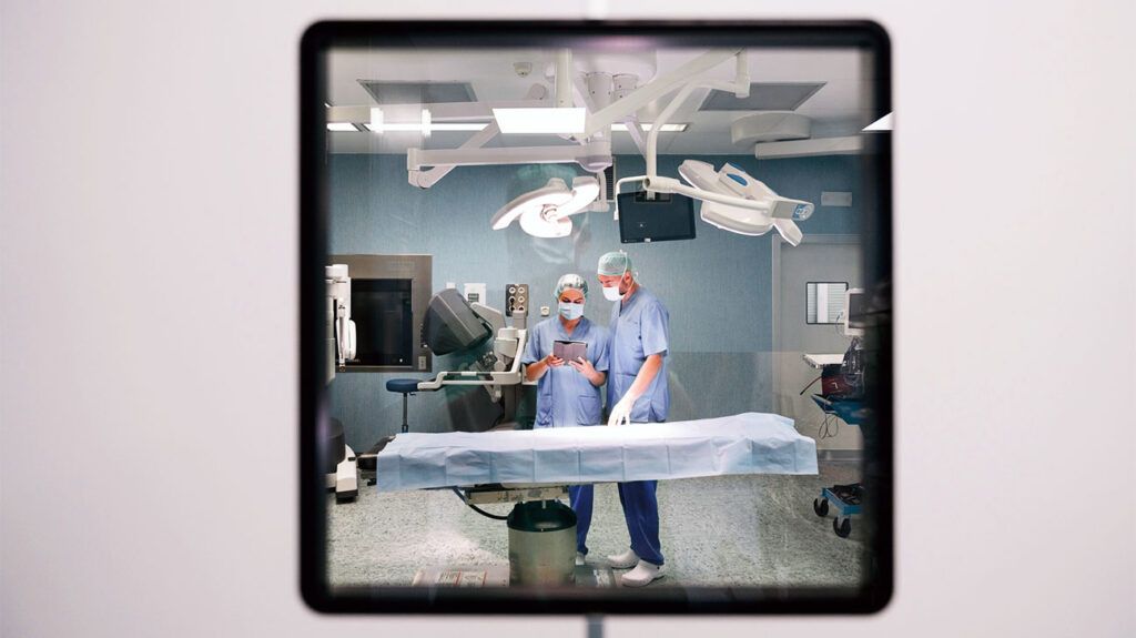 Two surgeons in an operating theatre looking at a document behind a glass window