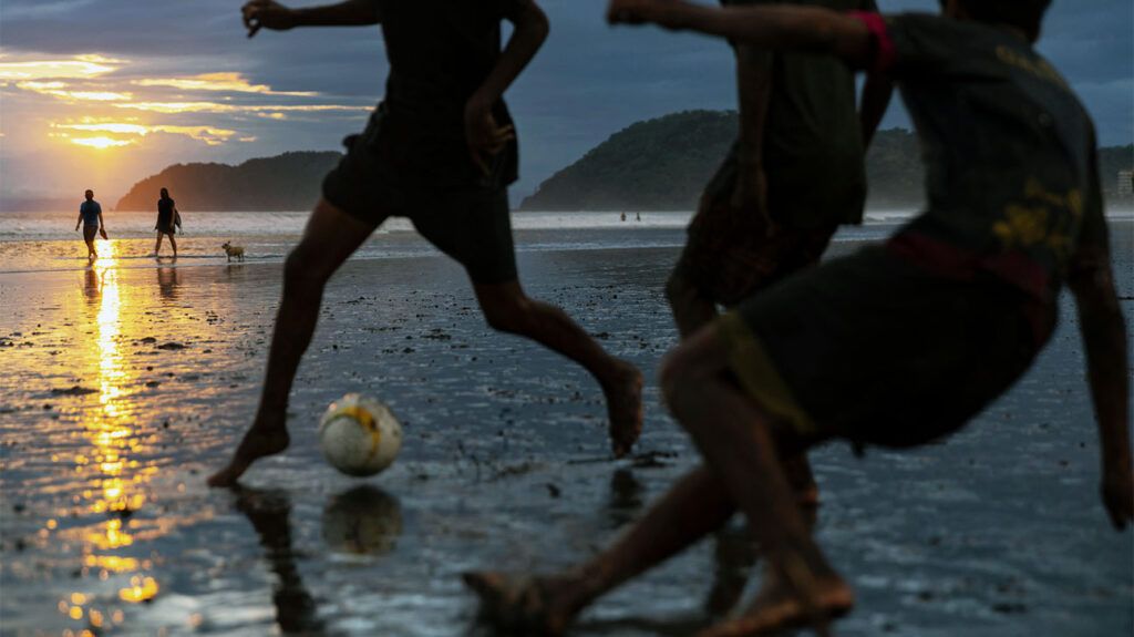 young people playing football on the beach at sunset