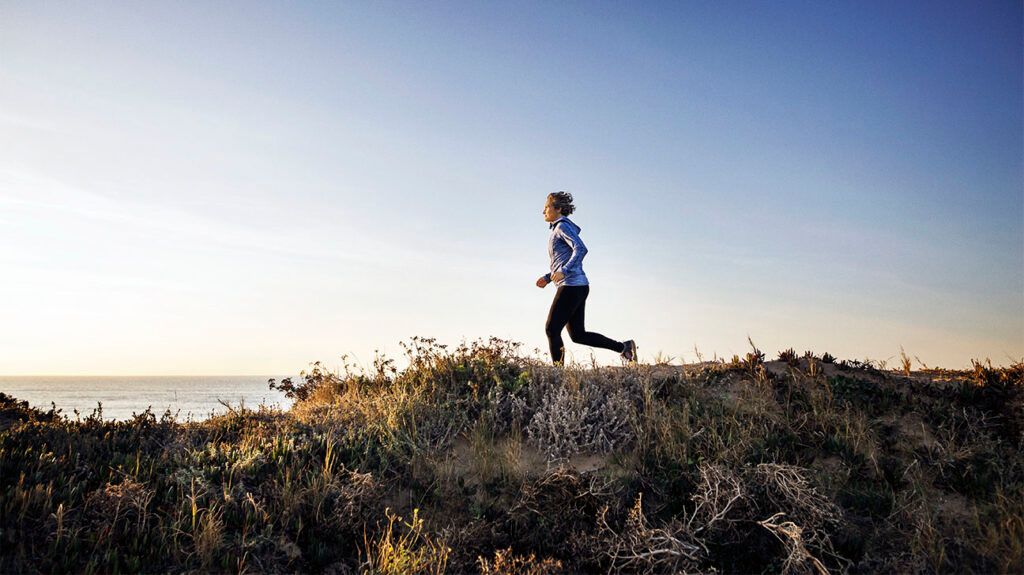 A woman jogging in a field against a backdrop of a clear sky