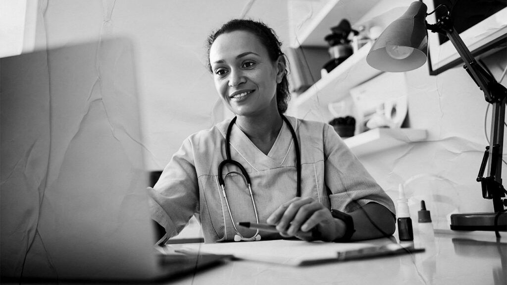 A doctor sat at a computer and typing while smiling.