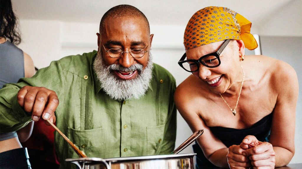 Two people laughing together and stirring a large pot in the kitchen.-2