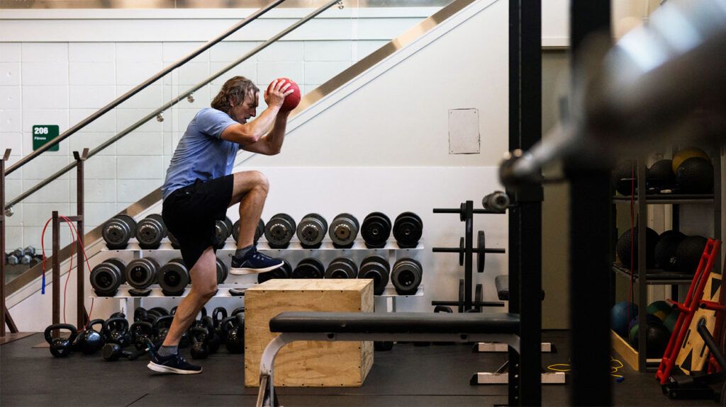 An older adult exercises with a medicine ball and box to step on in a gym