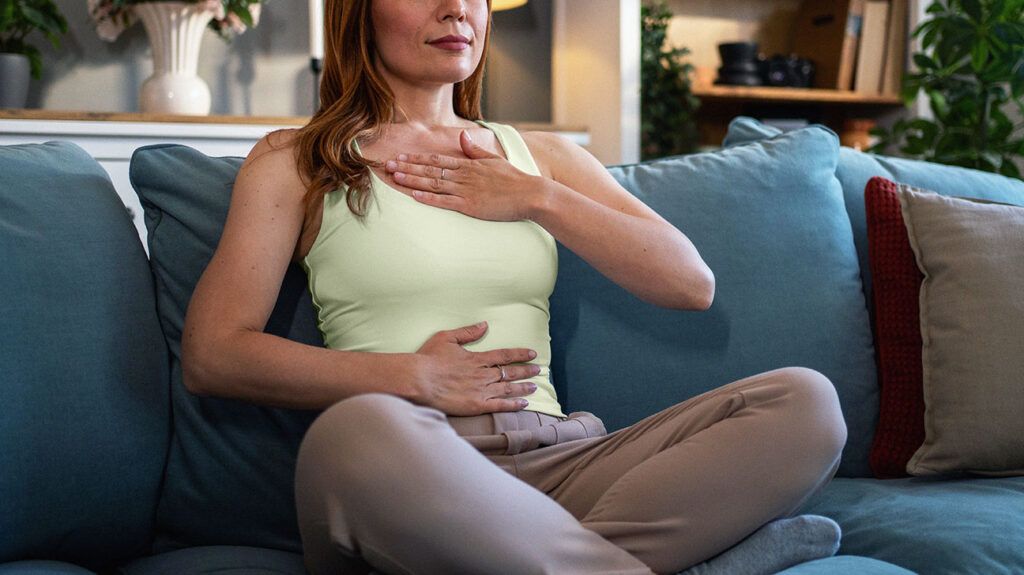 A person sat on a couch with their hands on their chest and abdomen.-3