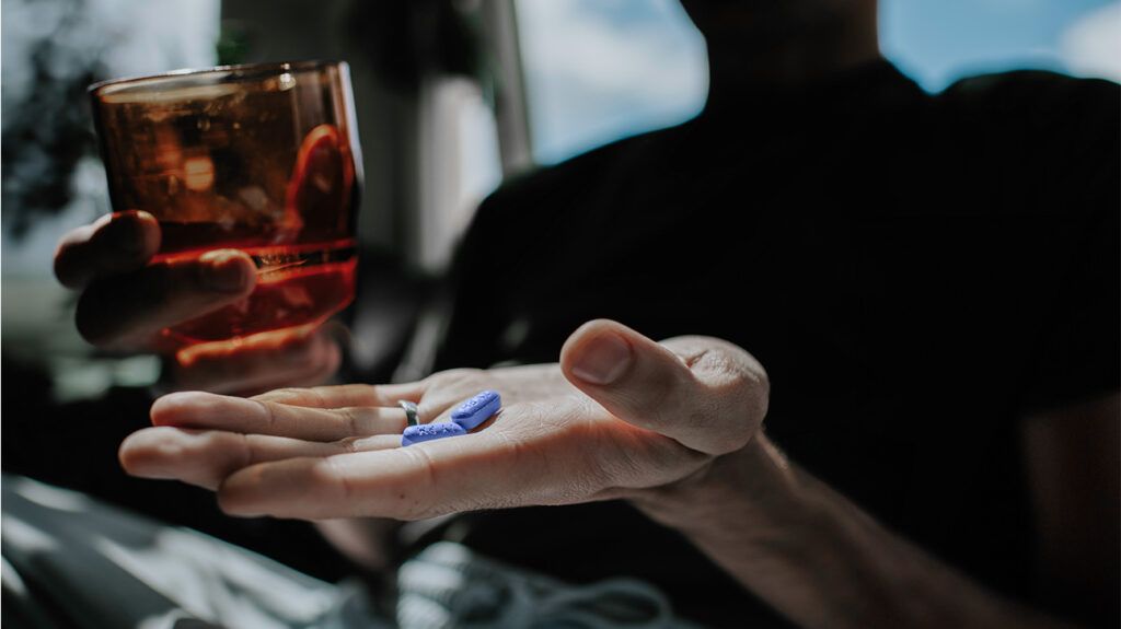 A hand holding two blue pills.-1