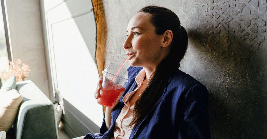 A woman drinking a red drink in a plastic cup.