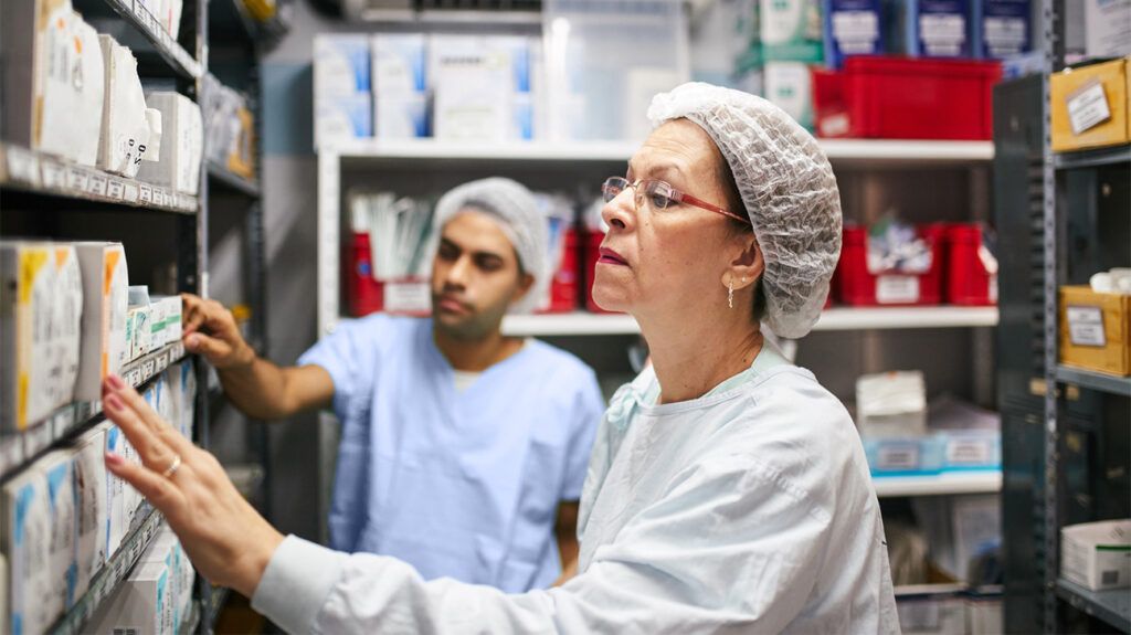 Two staff looking at boxes of medication on shelves at a pharmacy