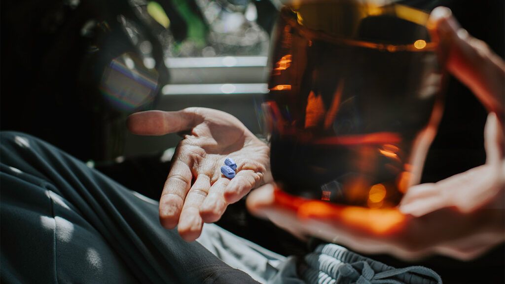 hands holding a cup of ice tea and two blue pills