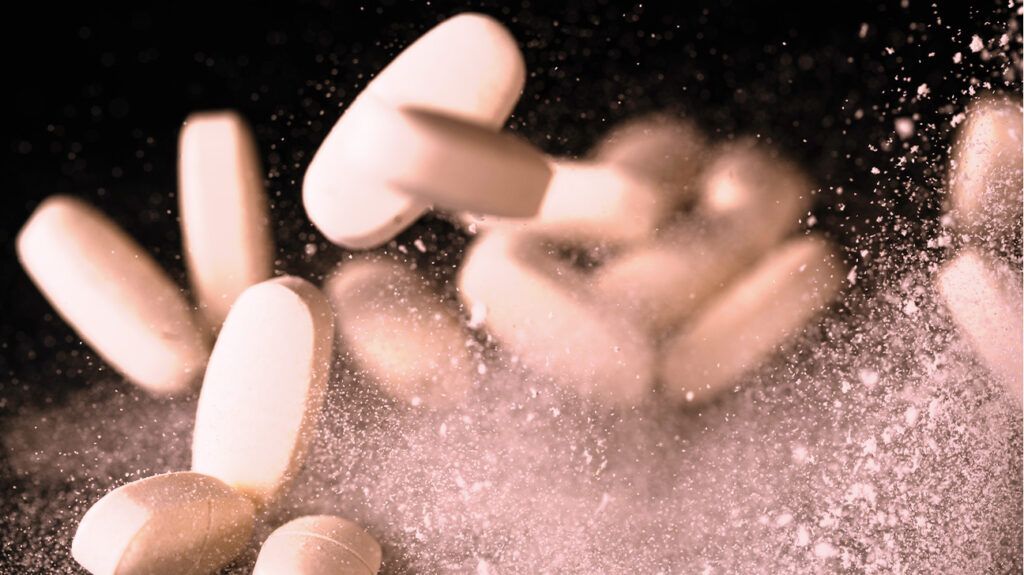 A handful of pills drop onto a surface, powder scattering as they touch the surface