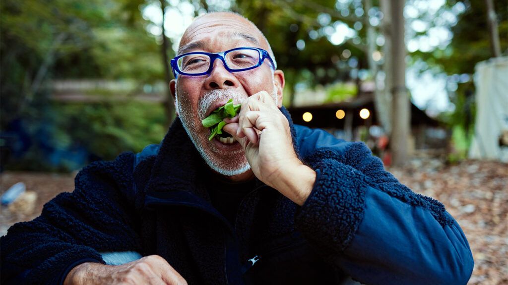 Older male sitting outside eating a salad with his hands