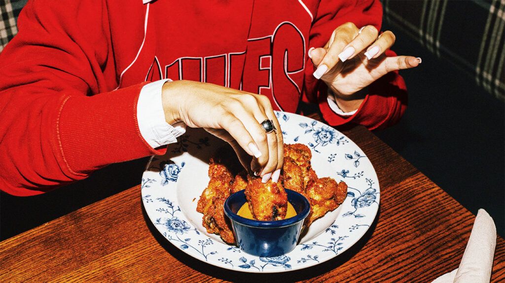 Hands dipping fried chicken into a pot of sauce.-2