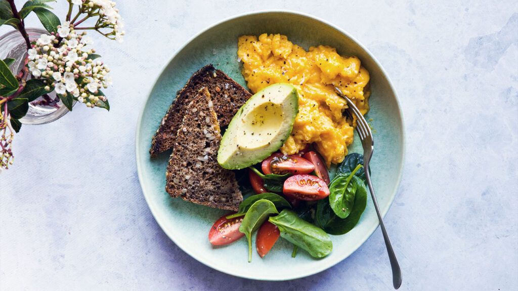 스크램블 에그, 씨앗 빵, 아보카도, 토마토, 시금치를 넣은 아침 식사