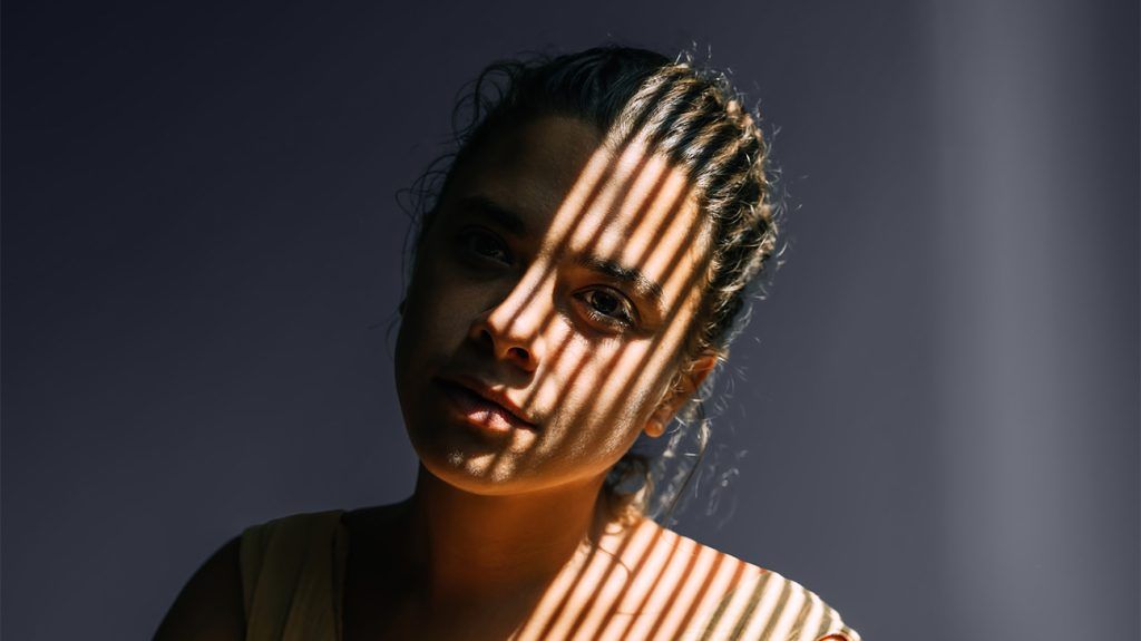 A window blind casts a shadow on a woman's face