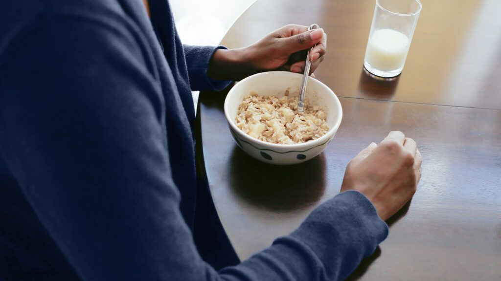 A person eating oatmeal with a glass of milk at a table