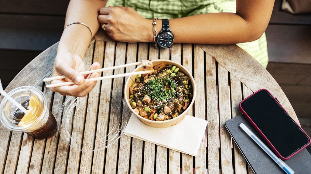 A person eating a healthy lunch outside using chopsticks.