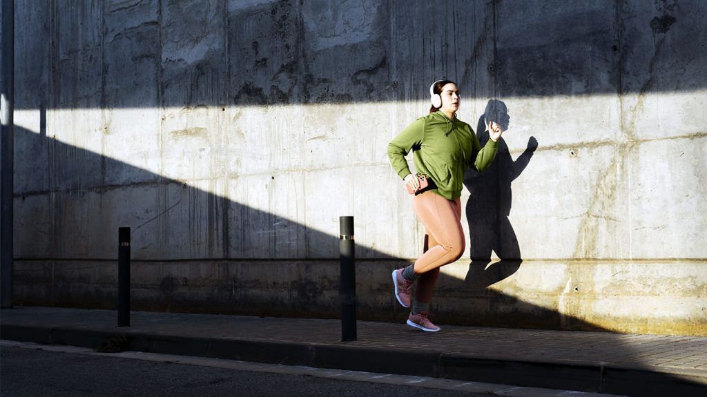 A female runner wearing headphones jogs along urban concrete wall during a morning workout session