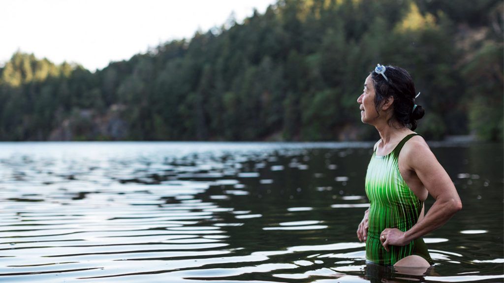 older East Asian woman standing in green bathing suit in a lake