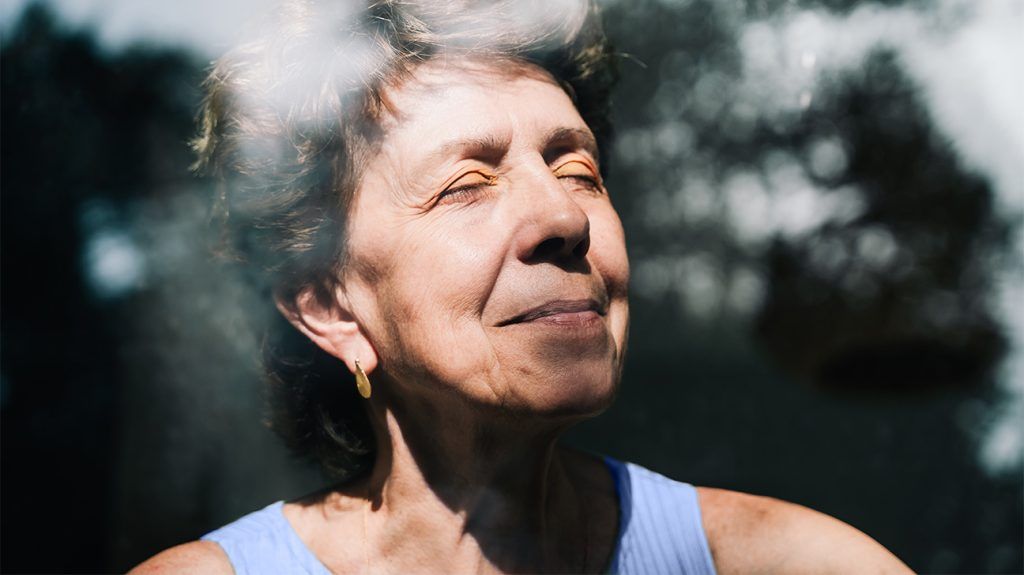 portrait of older white woman with her eyes closed by a window