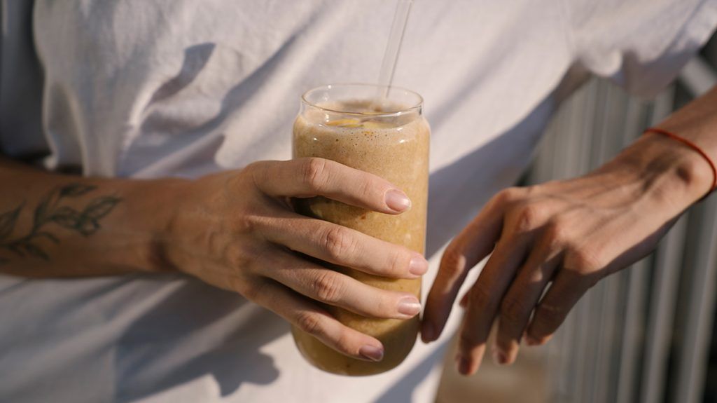 A close-up of a woman holding a glass full of a protein shake
