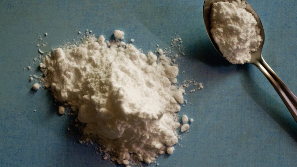 Creatine monohydrate in powder form on a flat surface and on a spoon